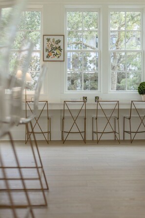 Een kamer met een groot raam, een ingelijste botanische print en een aantal stoelen met metalen frame.
