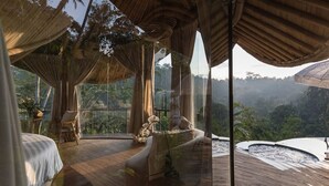 A luxurious room with a large bed, a seating area with a view of the forest, and a glass wall overlooking the landscape. - Belalu Bali Boutique & Spa Experience (Ubud)