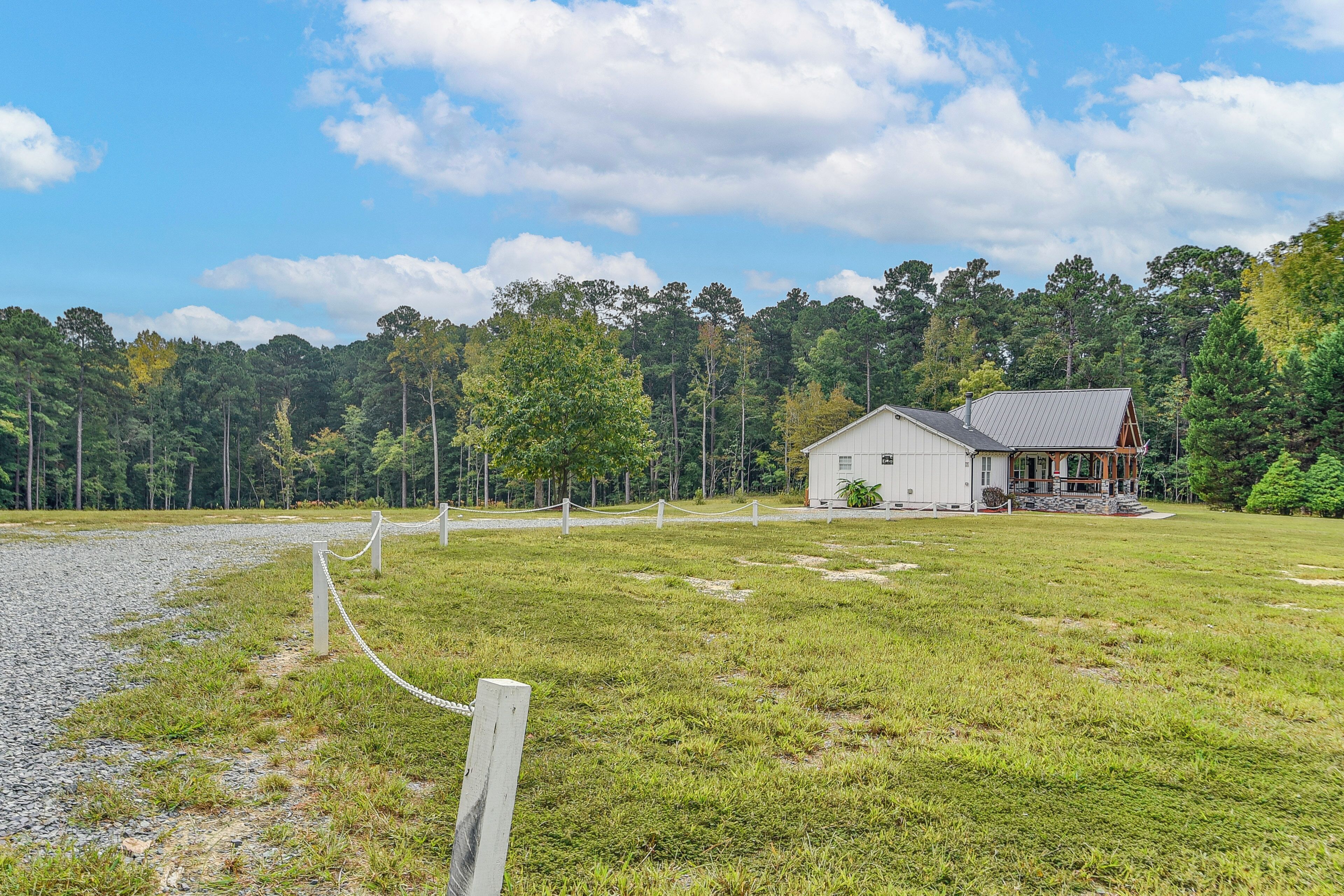 A house with a porch, surrounded by a grassy field and a forest.