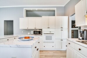 Een moderne keuken met witte kasten, een marmeren aanrecht, een magnetron, een oven en een koffiezetapparaat.