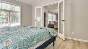 A bedroom with a bed, a window with blinds, and a door leading to another room.