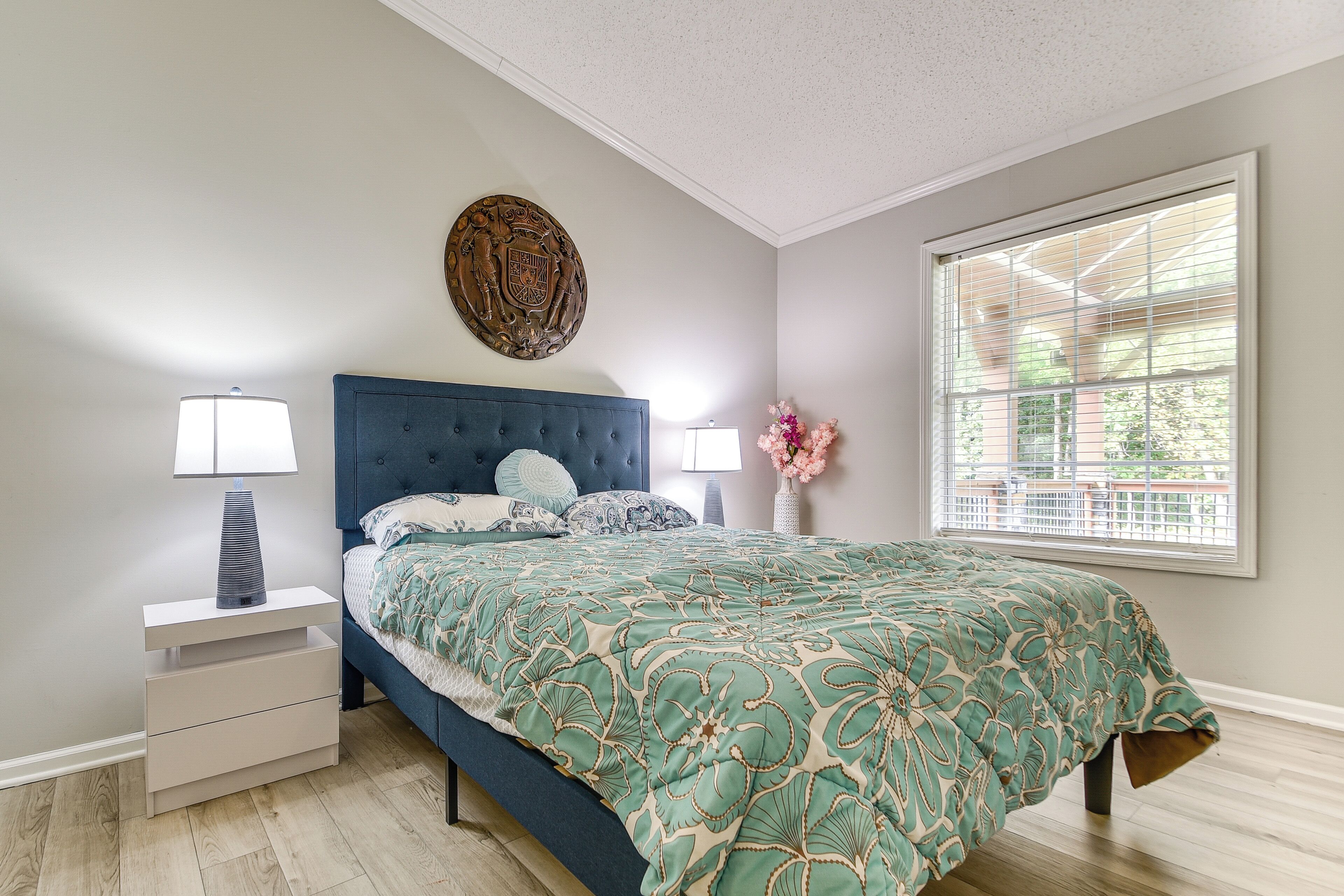 A bedroom with a bed, nightstands, a decorative wall piece, and a window with blinds.