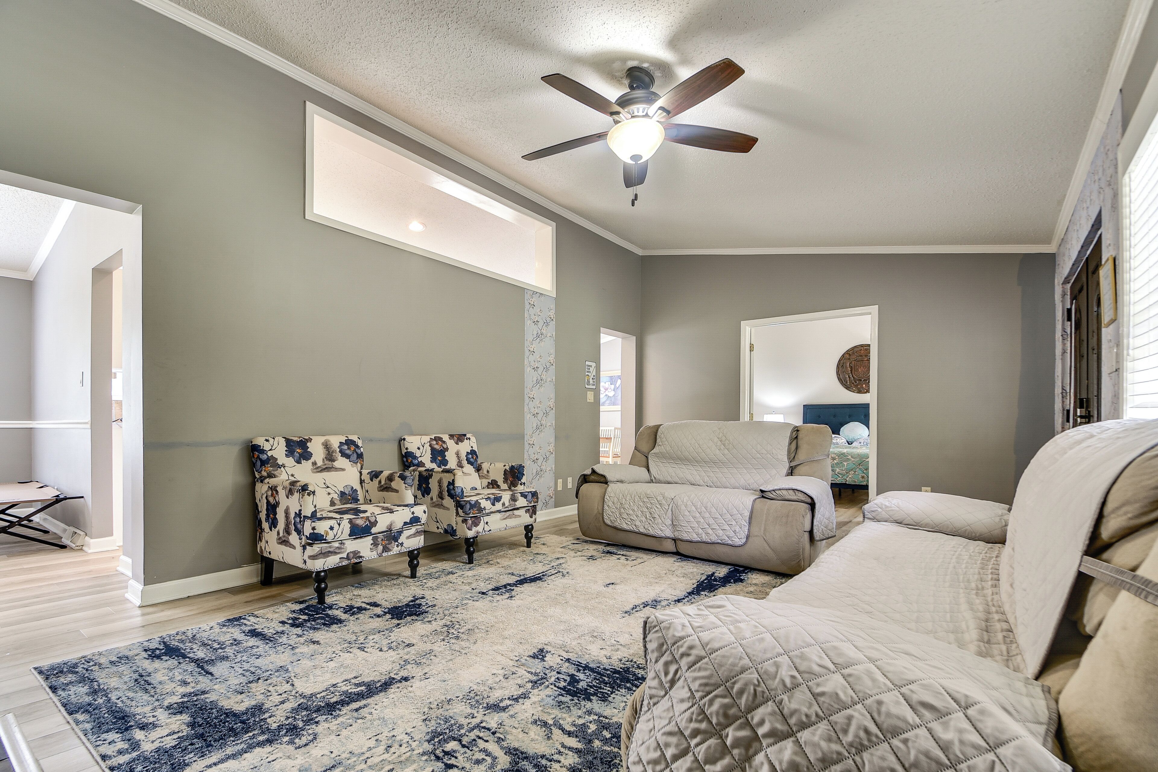 Un salon avec un ventilateur de plafond, une grande fenêtre, un tapis à motifs et un canapé.