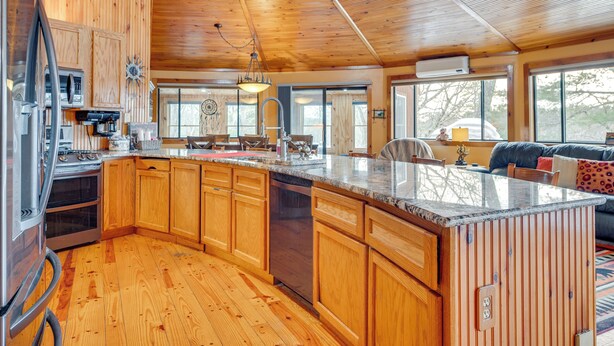 A spacious kitchen with wooden cabinets, a large island, and a dining area with a sofa and chairs. - Dock & Beach Access: Scenic Lake Ossipee Cabin! (Center Ossipee)