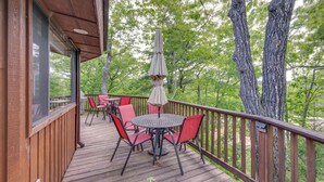 A wooden deck with a table and chairs, an umbrella, and a view of trees. - Dock & Beach Access: Scenic Lake Ossipee Cabin! (Center Ossipee)