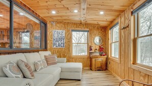 A cozy cabin interior with a sectional sofa, wooden walls, large windows, and a wooden ceiling. - Dock & Beach Access: Scenic Lake Ossipee Cabin! (Center Ossipee)