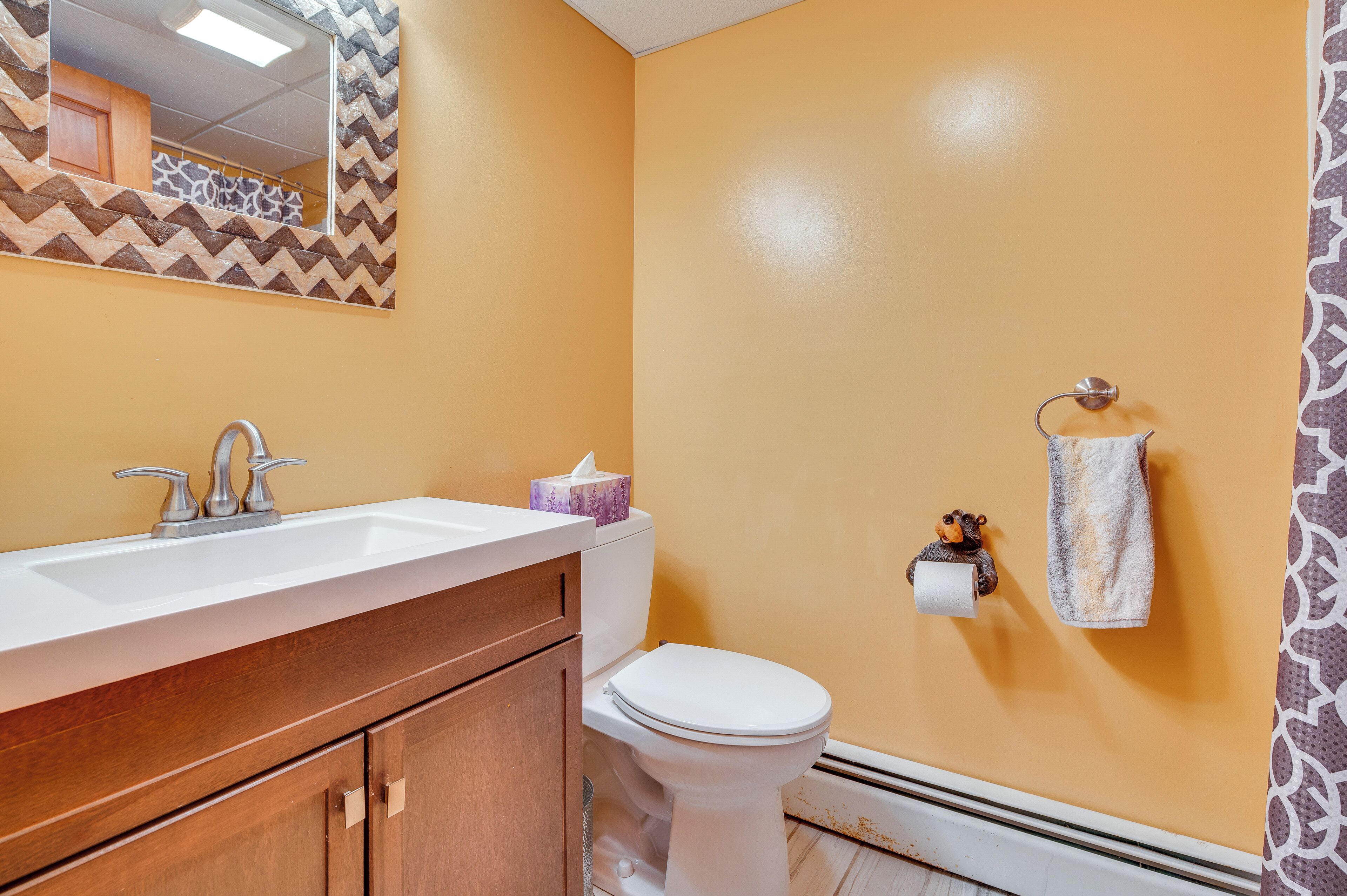 A bathroom with a wooden vanity, a white sink, a toilet, and a towel rack with a towel.
