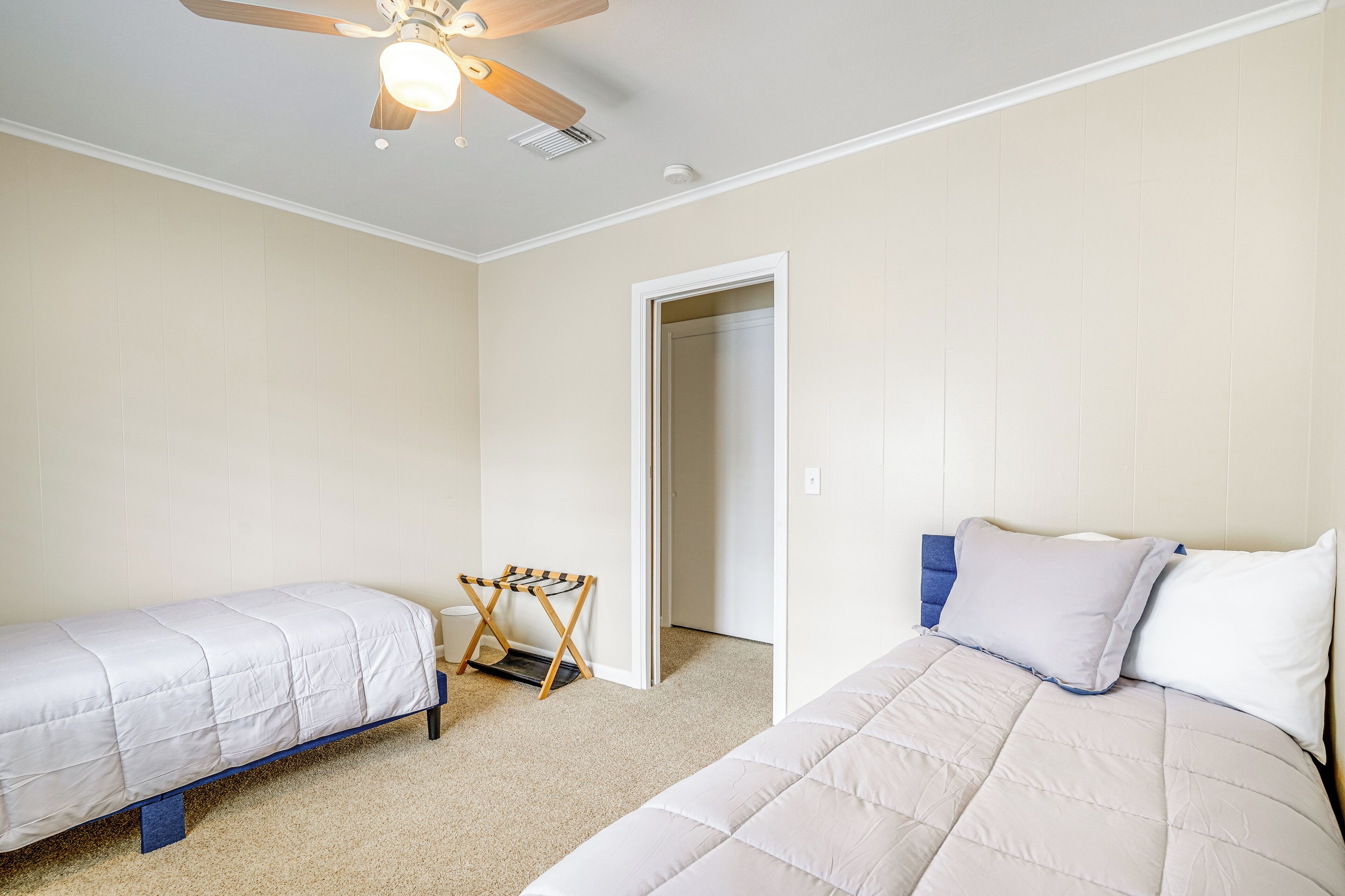 A bedroom with two single beds, a ceiling fan, and a door leading to another room.