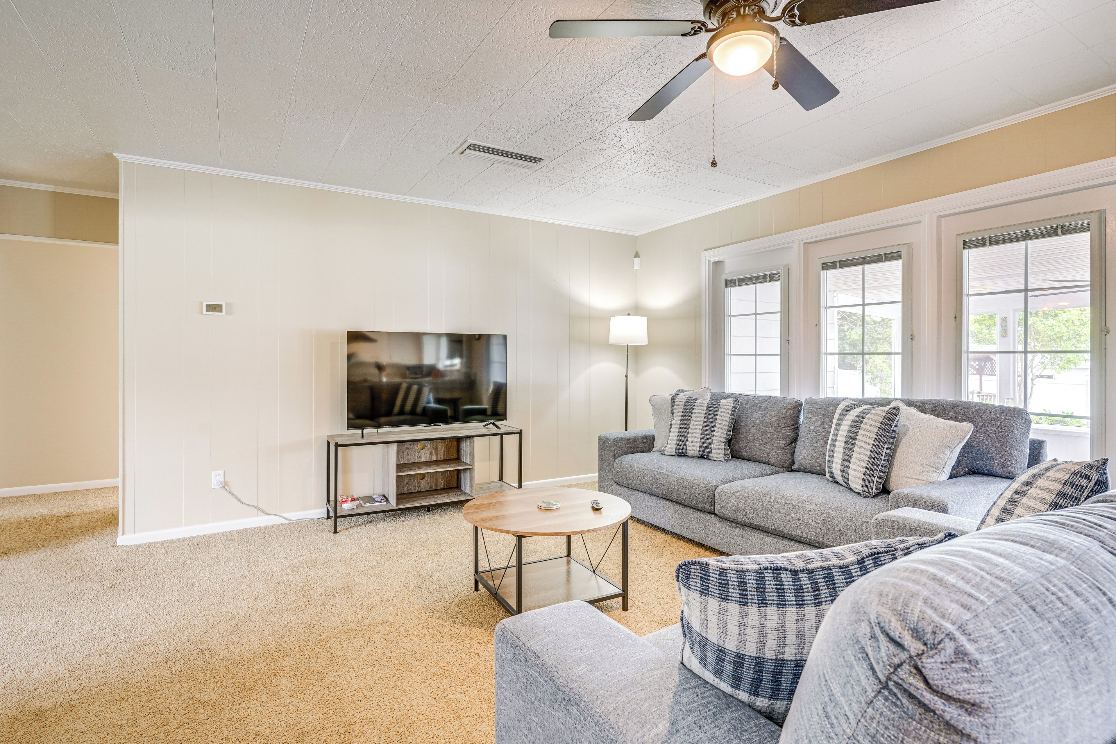 A living room with a gray sofa, a coffee table, a TV on a stand, and a ceiling fan.