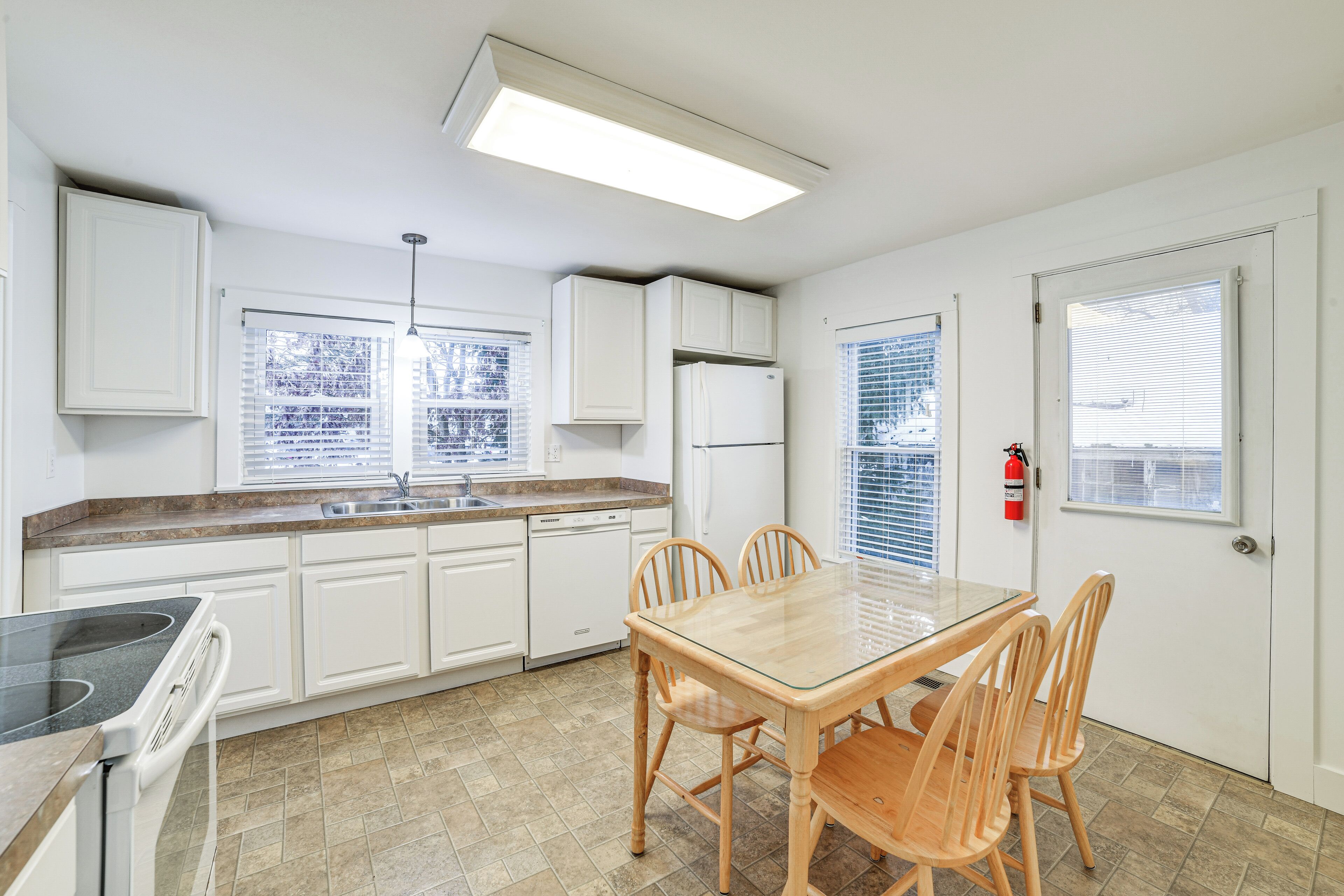 Una cocina con armarios blancos, lavavajillas, estufa y una mesa de comedor con sillas.