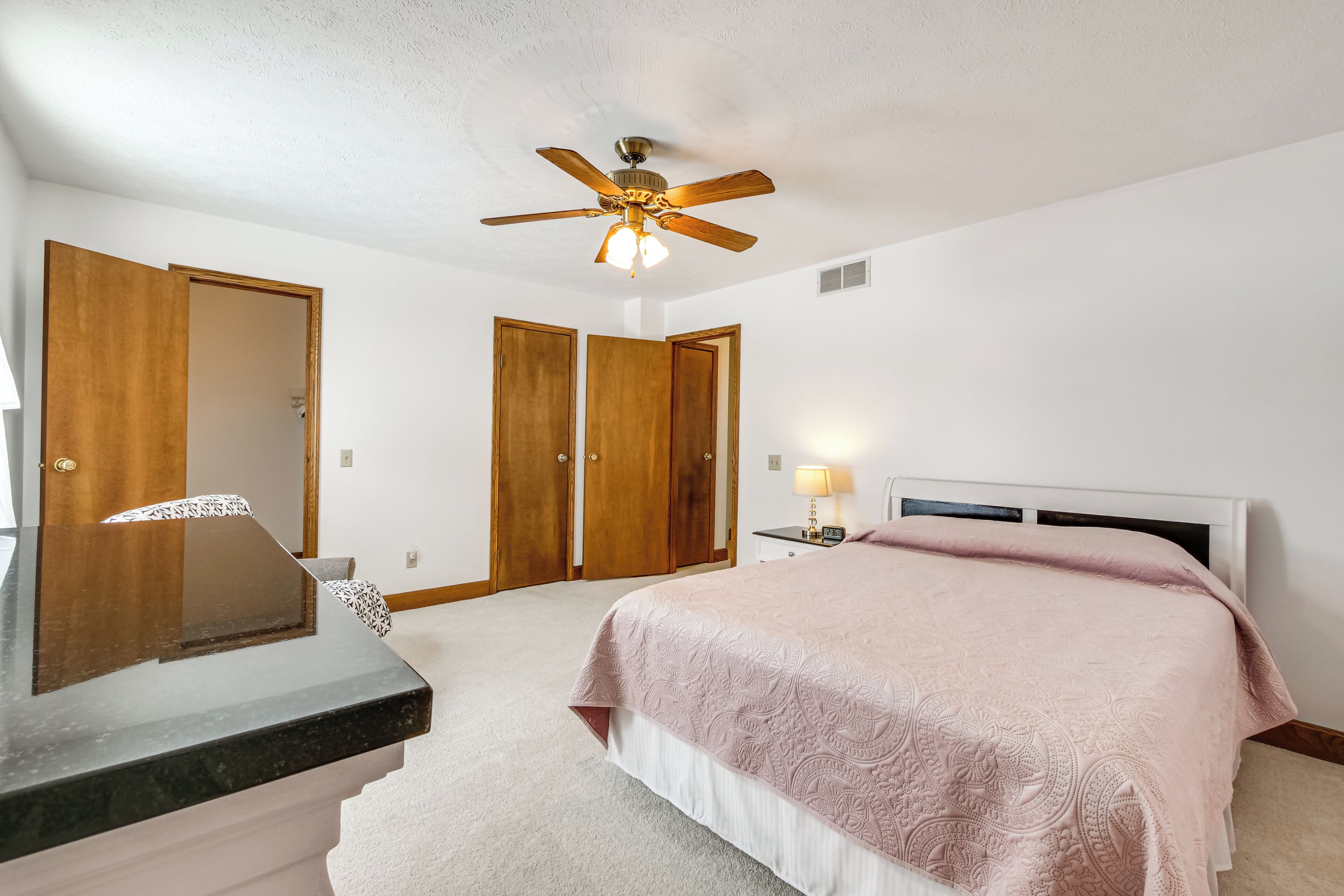 A bedroom with a bed, a desk, a ceiling fan, and two wooden doors.