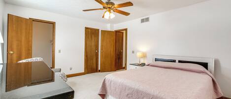 A bedroom with a bed, a desk, a ceiling fan, and two wooden doors.