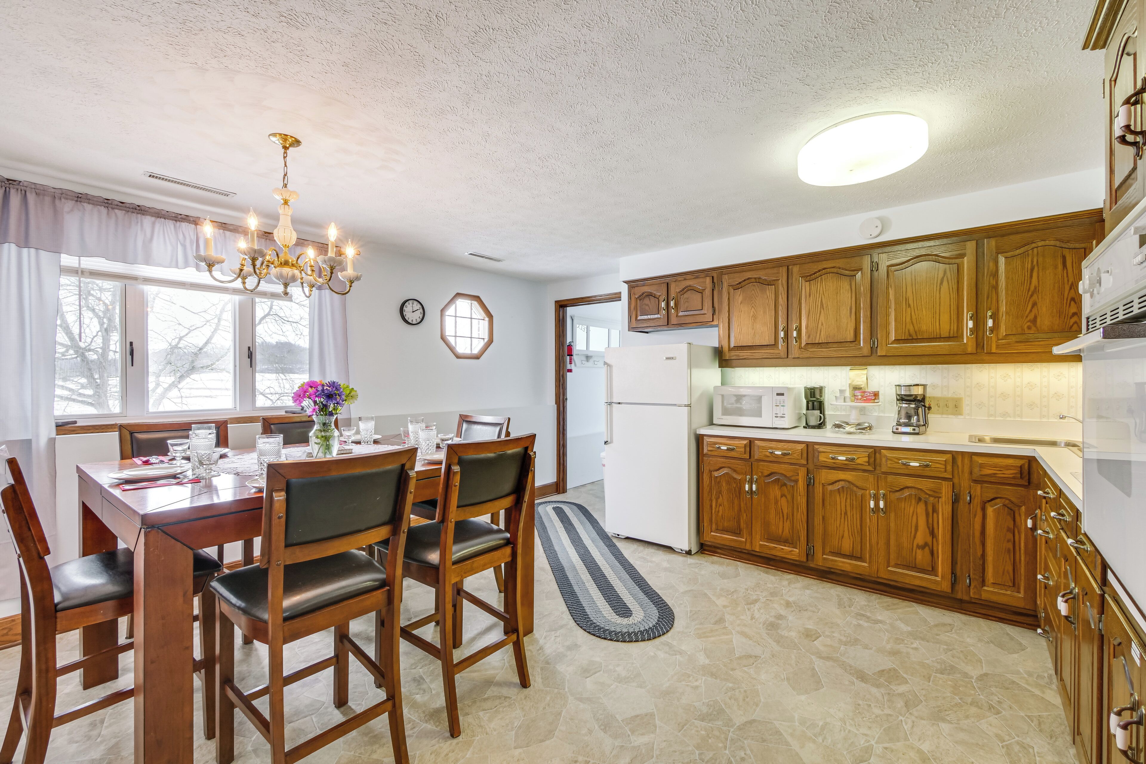 A kitchen with wooden cabinets, a dining table with chairs, a chandelier, and a refrigerator.