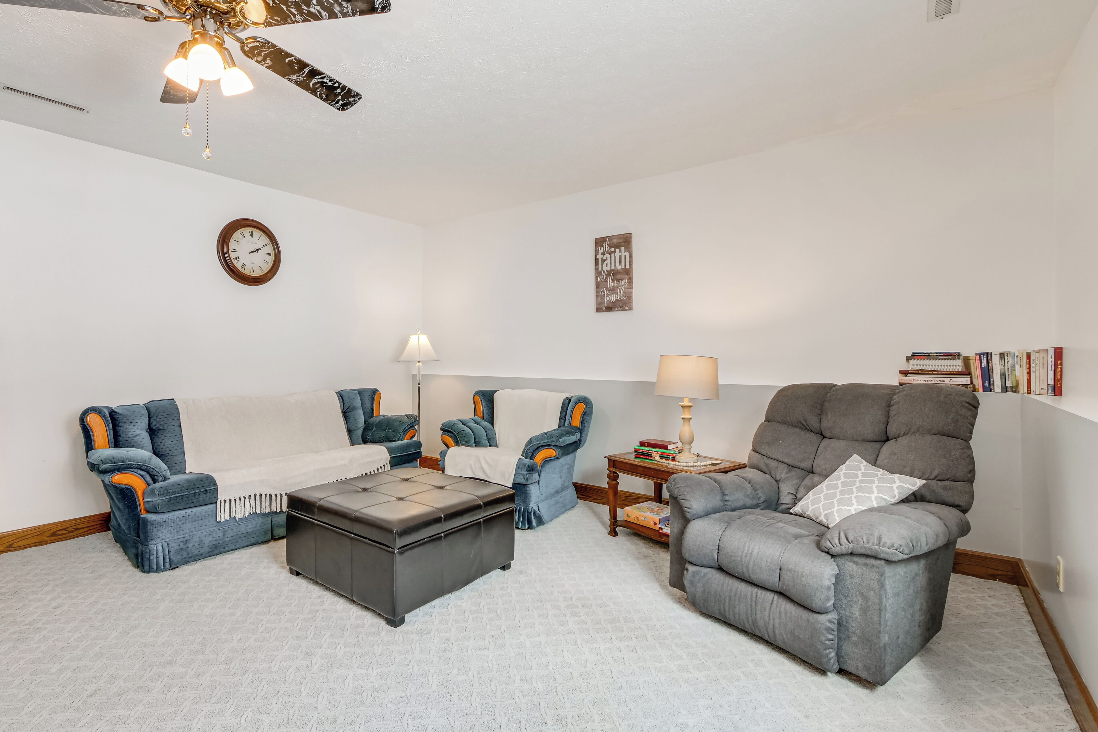 A living room with a sofa, two armchairs, a coffee table, a floor lamp, a clock, a wall decoration, and a bookshelf.