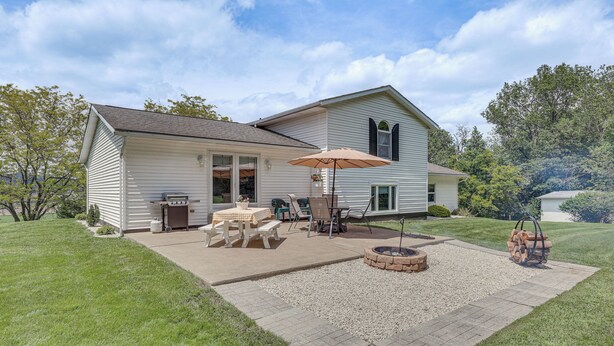 Een twee verdiepingen tellend huis met een patio, compleet met een tafel, stoelen, een vuurkorf en een barbecue.
