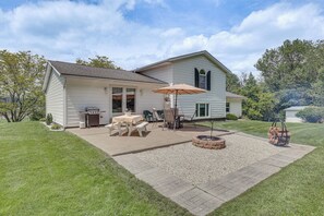 Een twee verdiepingen tellend huis met een patio, compleet met een tafel, stoelen, een vuurkorf en een barbecue.