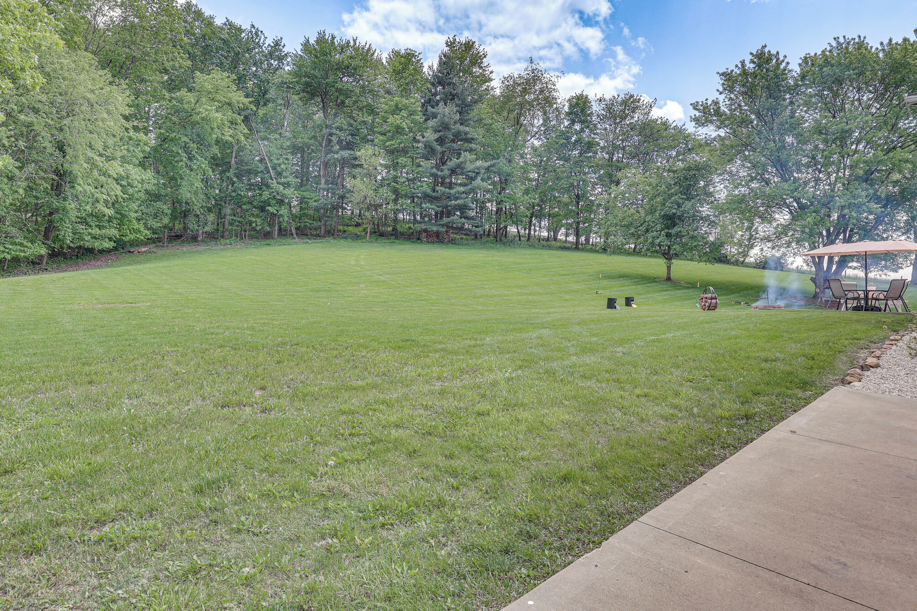 A large, well-maintained grassy yard with a fire pit and outdoor furniture, surrounded by trees.