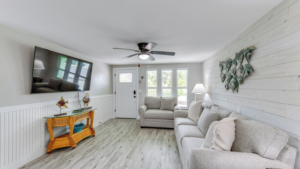A living room with a ceiling fan, a television mounted on the wall, a sofa, a coffee table, and a door leading to another room. - 2 Blocks to Beach: Tropical Retreat in Anna Maria (Anna Maria)