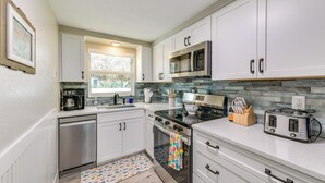 A modern kitchen with white cabinets, stainless steel appliances, and a window providing natural light. - 2 Blocks to Beach: Tropical Retreat in Anna Maria (Anna Maria)