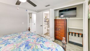 A bedroom with a bed, a ceiling fan, a dresser, a TV, and a bathroom door. - 2 Blocks to Beach: Tropical Retreat in Anna Maria (Anna Maria)