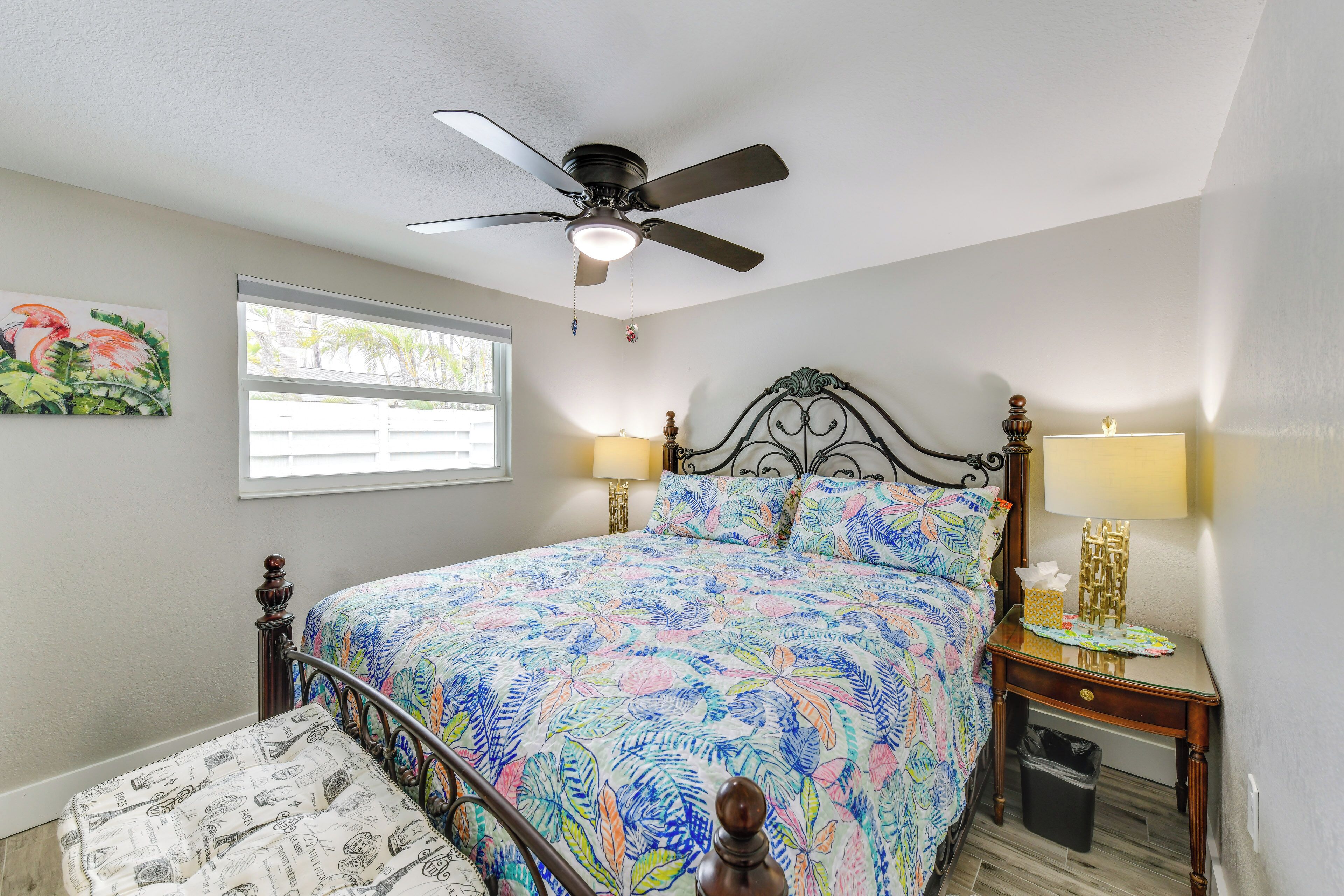 A bedroom with a bed, a ceiling fan, a window, a nightstand, and a trash can.