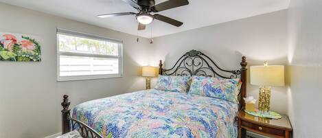 A bedroom with a bed, a ceiling fan, a window, a nightstand, and a trash can.