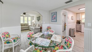 A dining area with a glass table surrounded by floral chairs, a ceiling fan, and a view into a living room with a sofa and a plant. - 2 Blocks to Beach: Tropical Retreat in Anna Maria (Anna Maria)