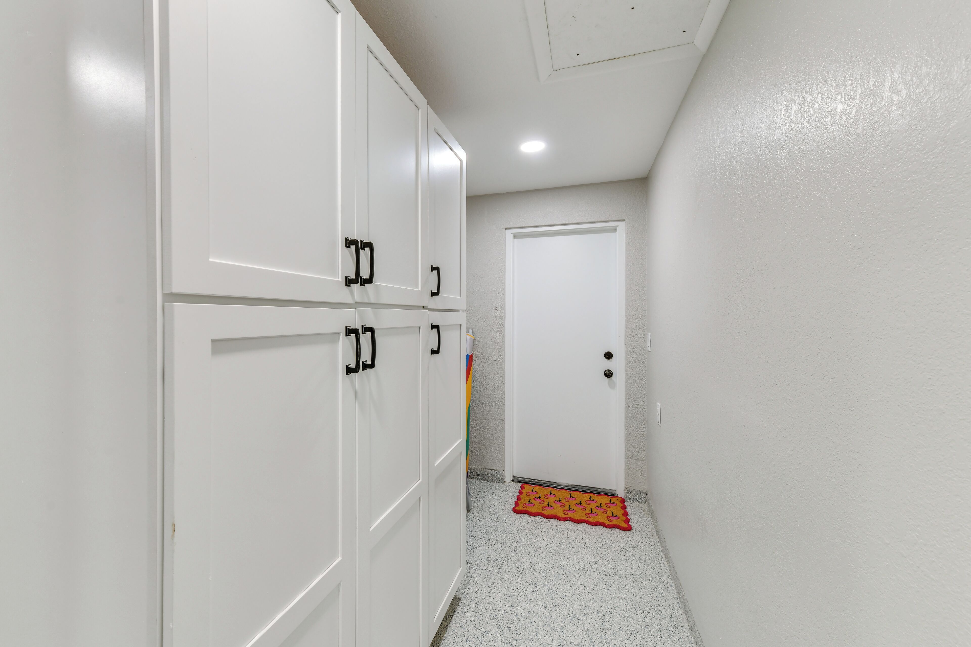 A hallway with white lockers, a door, and a colorful mat on the floor.
