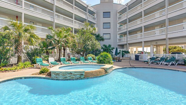 Ett hotell med poolområde, flera balkonger och palmer.