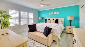 A bedroom with a bed, bedside tables, a ceiling fan, and a window with blinds. - Walk to Ocean: Carolina Beach Condo w/ 2 Balconies (Carolina Beach)