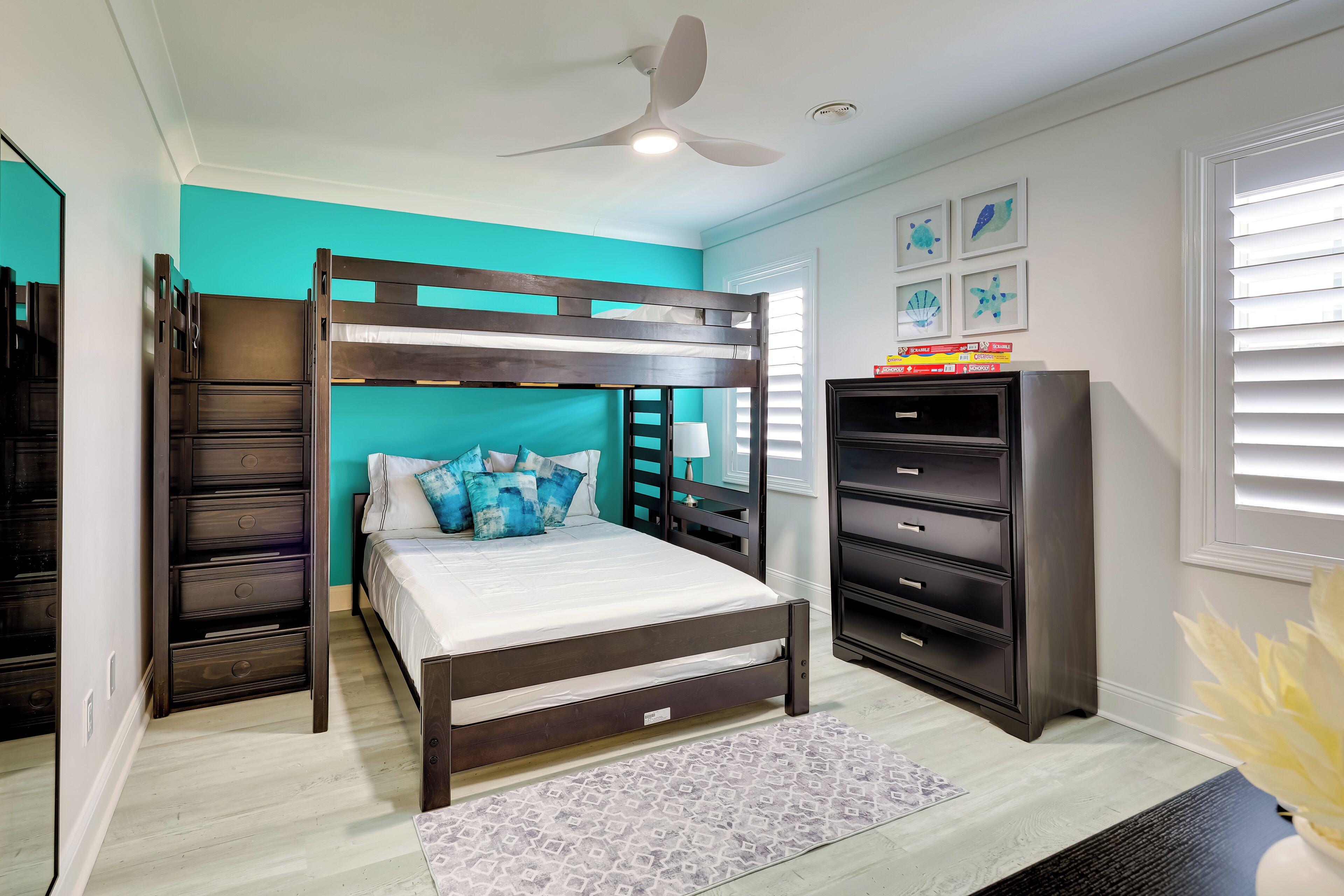 Ein Schlafzimmer mit Etagenbett, Kommode, Deckenventilator und Bildern an der Wand.