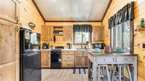 A wooden cabin kitchen with a refrigerator, stove, sink, and bar stools. - 'bluebird Treehouse' Near Kiamichi Mtns w/ Hot Tub (Talihina)