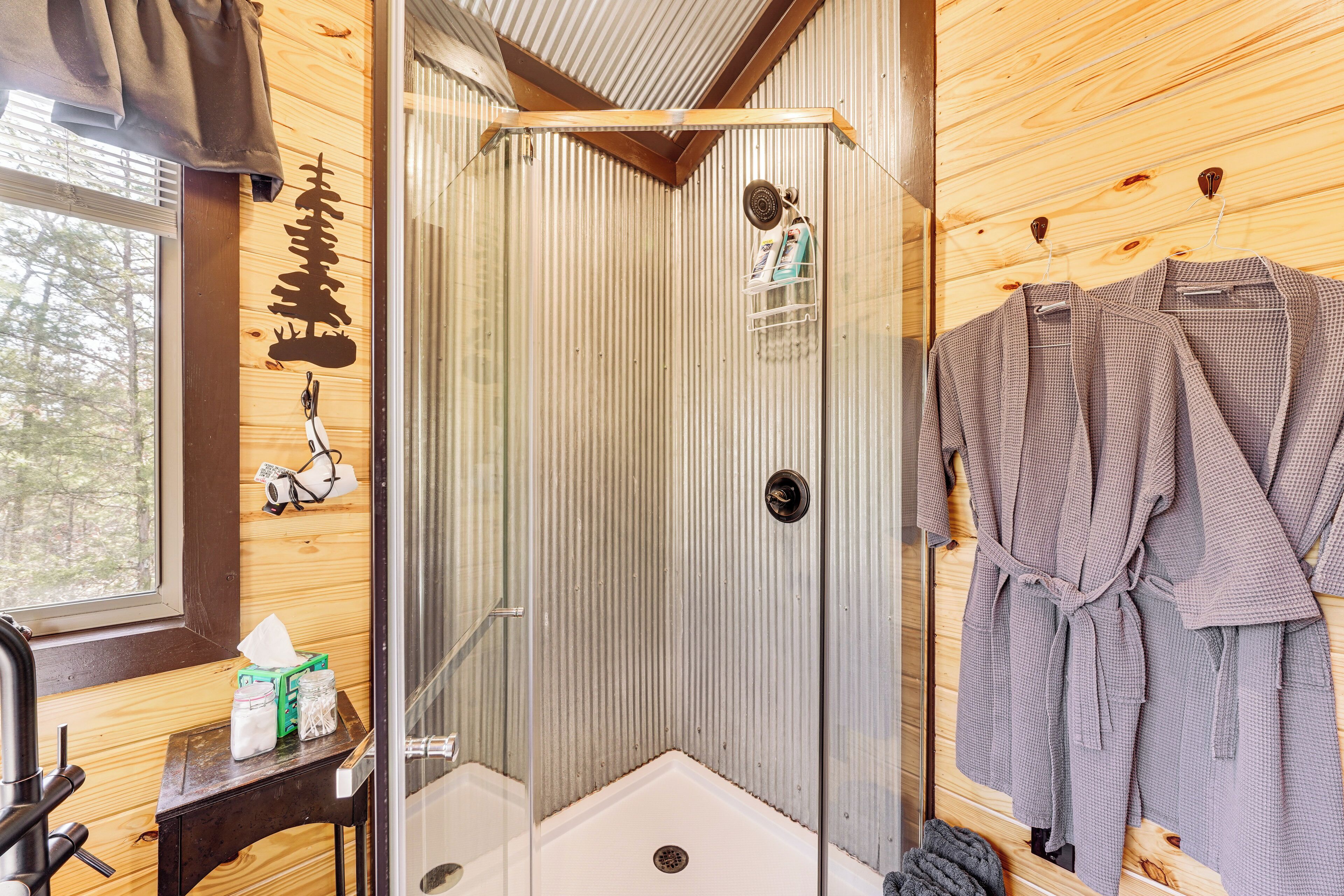 A shower with a glass door, wooden walls, and a towel rack with robes.