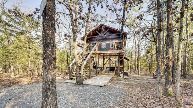 A wooden cabin with a staircase and deck, surrounded by trees. - 'bluebird Treehouse' Near Kiamichi Mtns w/ Hot Tub (Talihina)