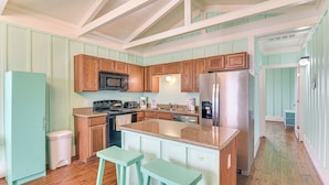 Una cocina con armarios de madera, encimera de granito, refrigerador de acero inoxidable y un cubo de basura blanco.