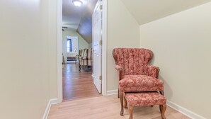 A hallway with a wooden floor, a red upholstered chair, and a white door leading to another room. - Hike, Golf & Boat: Wake Forest Home w/ Yard (Wake Forest)