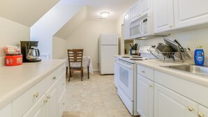 A kitchen with white cabinets, a microwave, a refrigerator, and a sink. There is a chair and a table with a white tablecloth. - Hike, Golf & Boat: Wake Forest Home w/ Yard (Wake Forest)