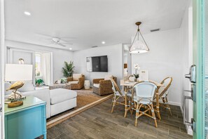 A modern living room with a sofa, dining table, chairs, a TV, and a ceiling fan.