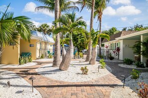 A courtyard with palm trees, a brick pathway, and a building with a sign.