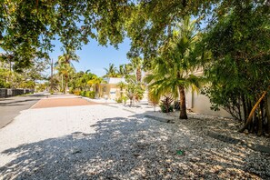 Uma área residencial com entrada pavimentada, caminho de cascalho, palmeiras e um edifício com fachada bege.