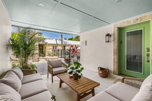A covered patio area with a sofa, a wooden table, and potted plants.