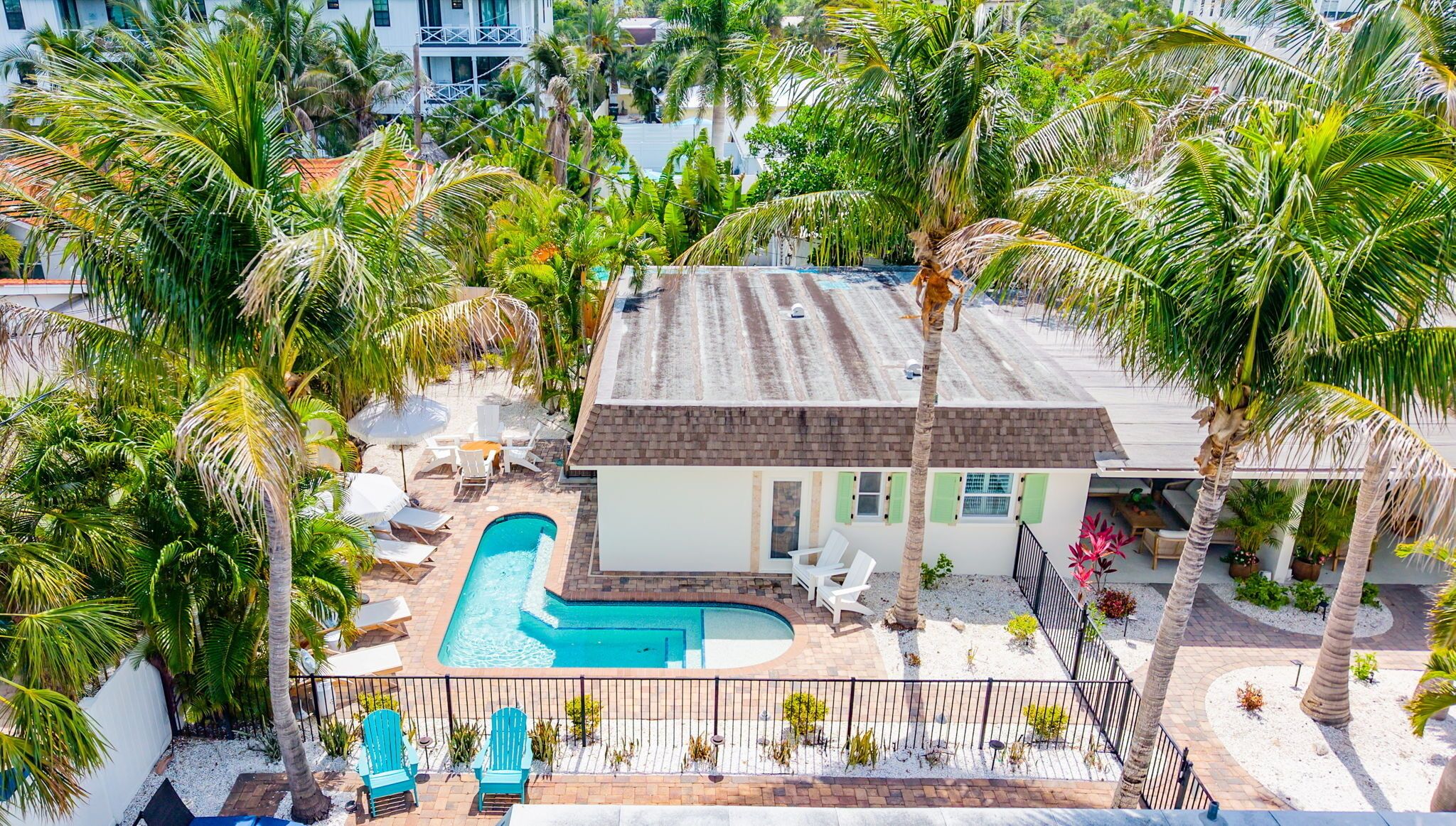 A house with a swimming pool, surrounded by palm trees and a fenced patio area.