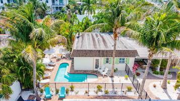 A house with a swimming pool, surrounded by palm trees and a fenced patio area.