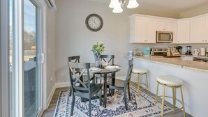 A modern kitchen with white cabinets, a stainless steel microwave, and a dining area with a round table and chairs. - Stay & Play: Spacious Concord Townhome Near Uptown (Concord)