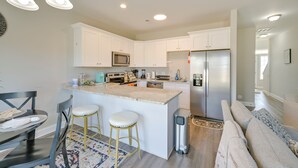 A modern kitchen with white cabinets, a stainless steel refrigerator, and a central island with stools. - Stay & Play: Spacious Concord Townhome Near Uptown (Concord)
