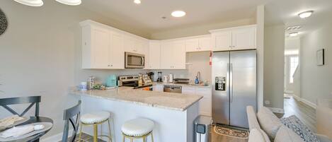 A modern kitchen with white cabinets, a stainless steel refrigerator, and a central island with stools.