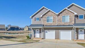 A two-story residential building with a stone facade, two garages, and a paved driveway. - Stay & Play: Spacious Concord Townhome Near Uptown (Concord)