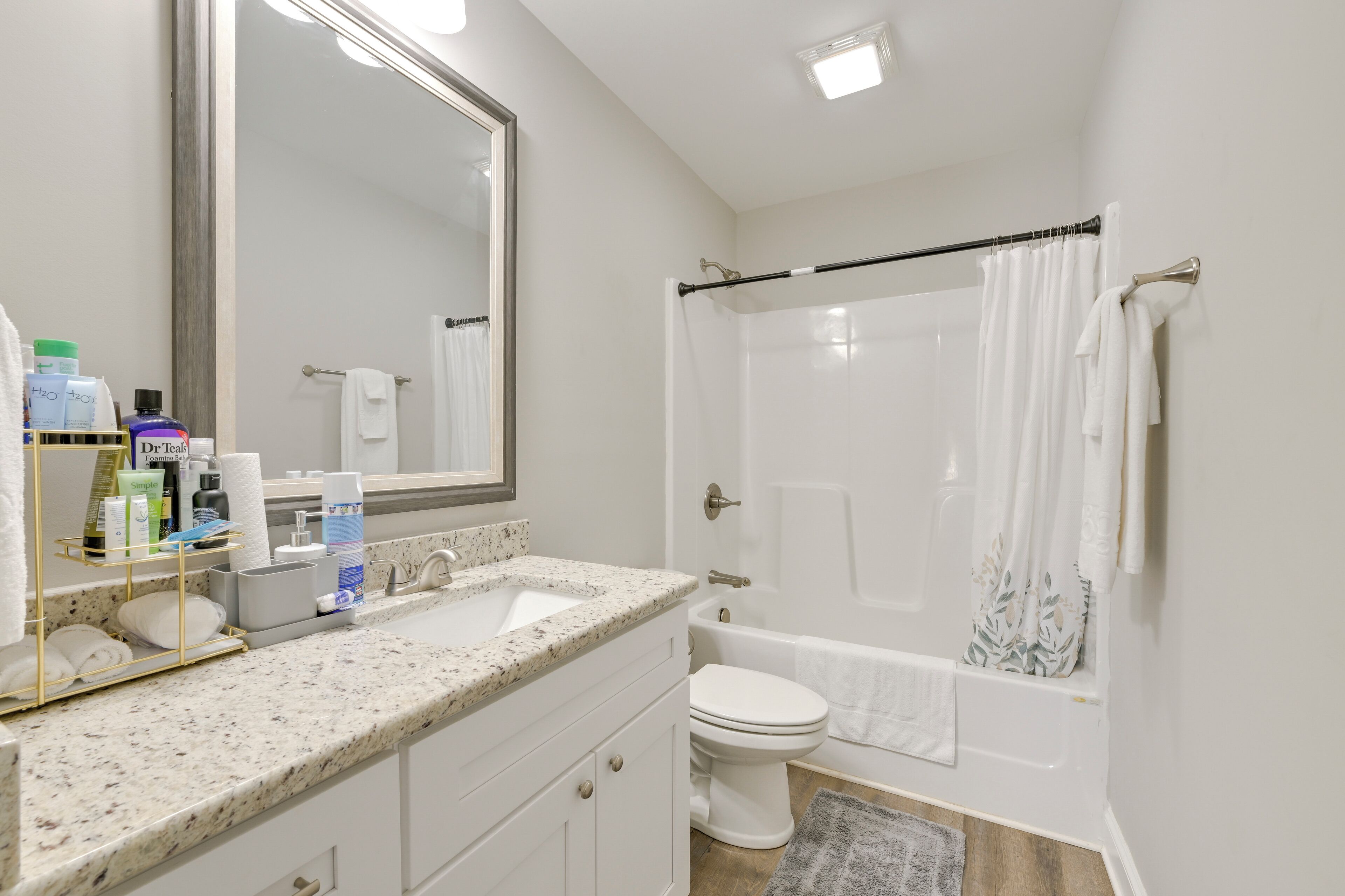 A bathroom with a sink, toilet, and bathtub. There are toiletries on the counter and a towel rack.
