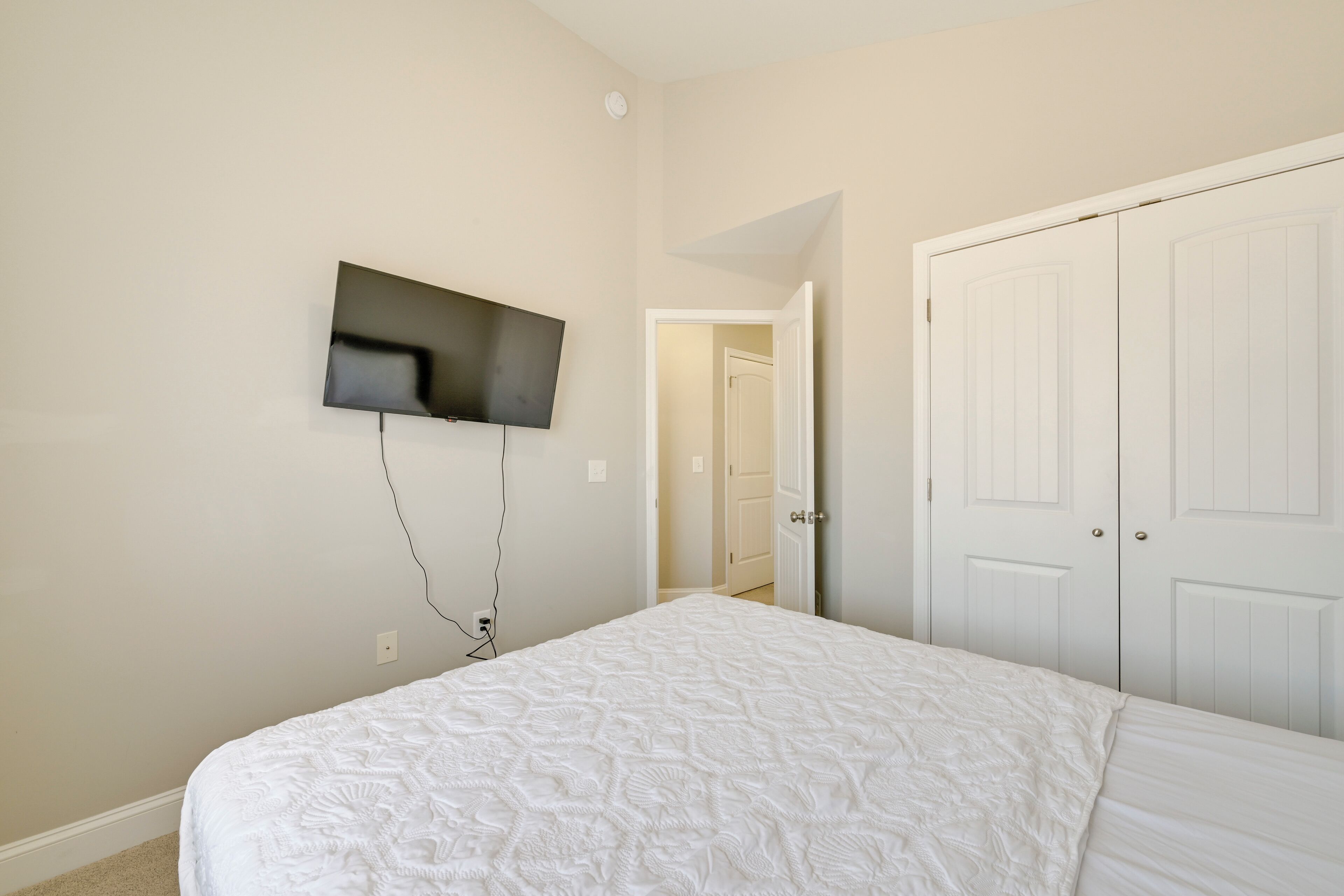 Une chambre à coucher avec un lit, un téléviseur fixé au mur et une porte blanche.