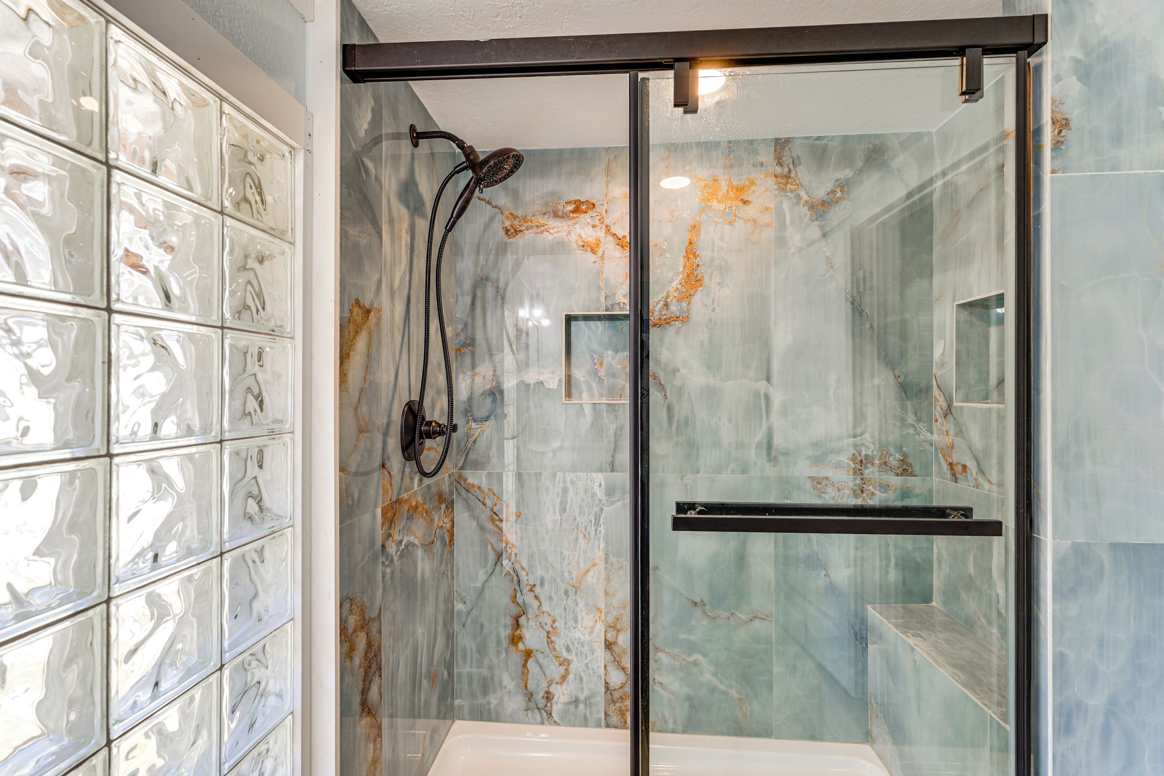 A modern bathroom with a glass shower enclosure, marble walls, and a glass shower door.